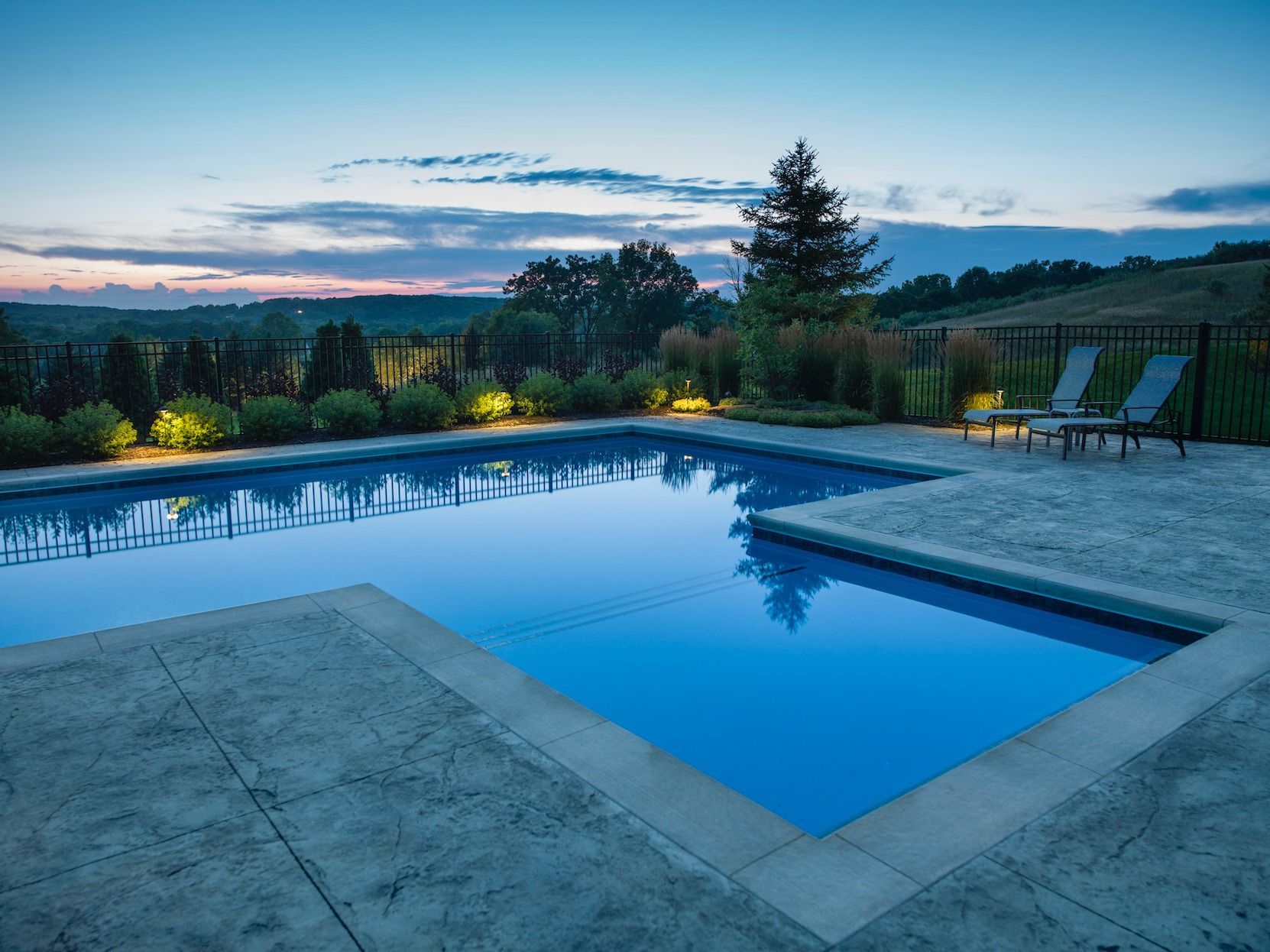 Backyard infinity pool at dusk with lounge chairs and scenic sunset view