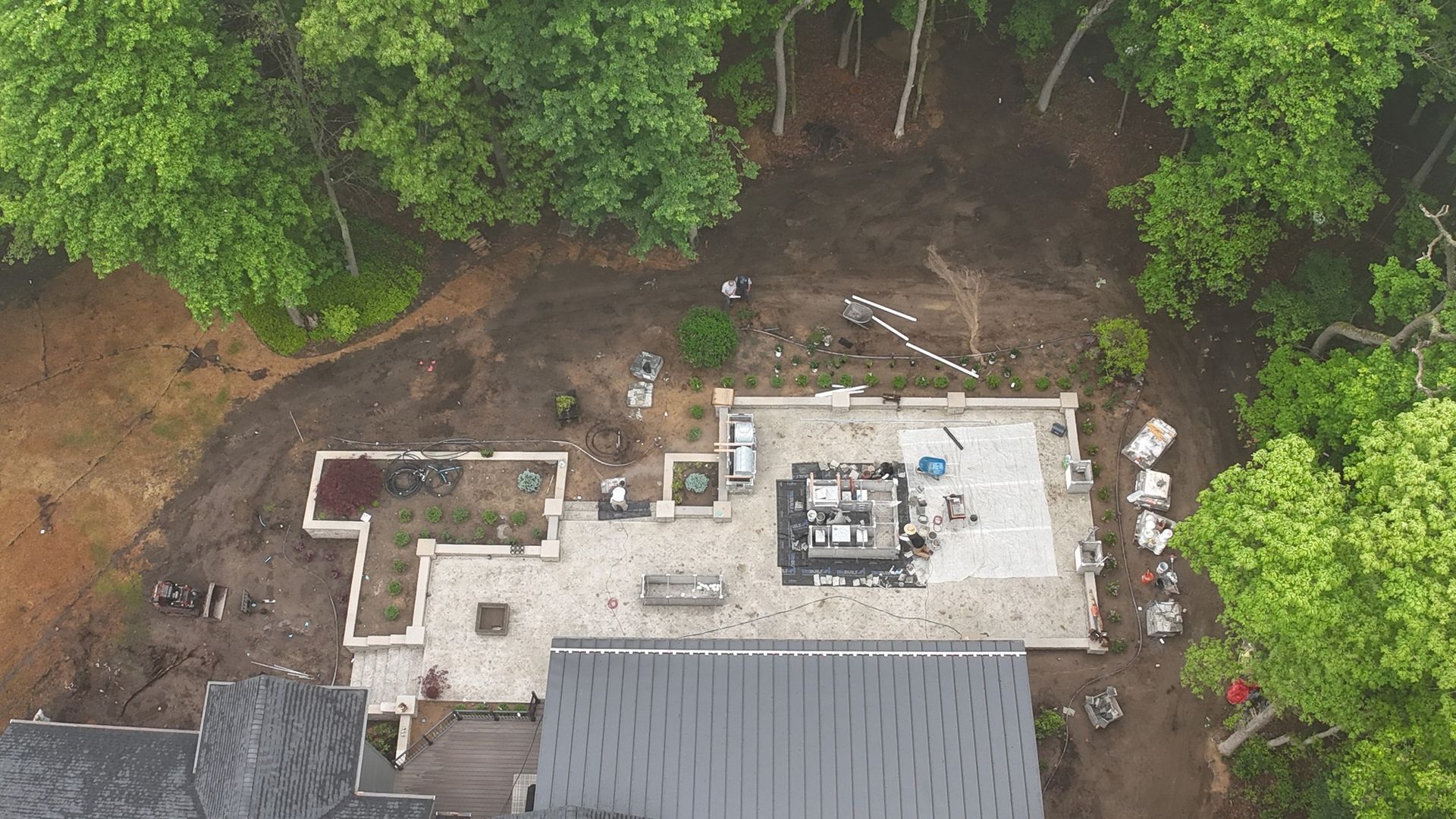 Aerial view of a white-roofed house under construction beside dense green trees.