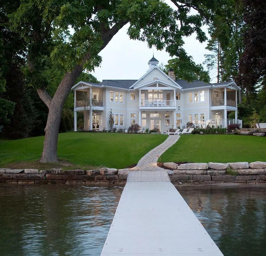 Grand waterfront mansion with a white dock leading from the lake to a manicured lawn.