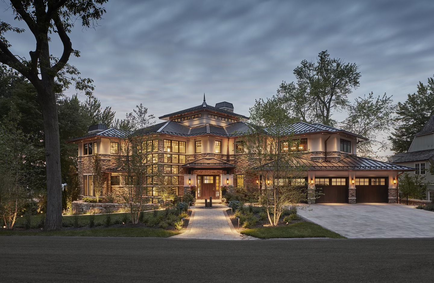 Elegant large lit house at dusk with trees and a glowing front entrance