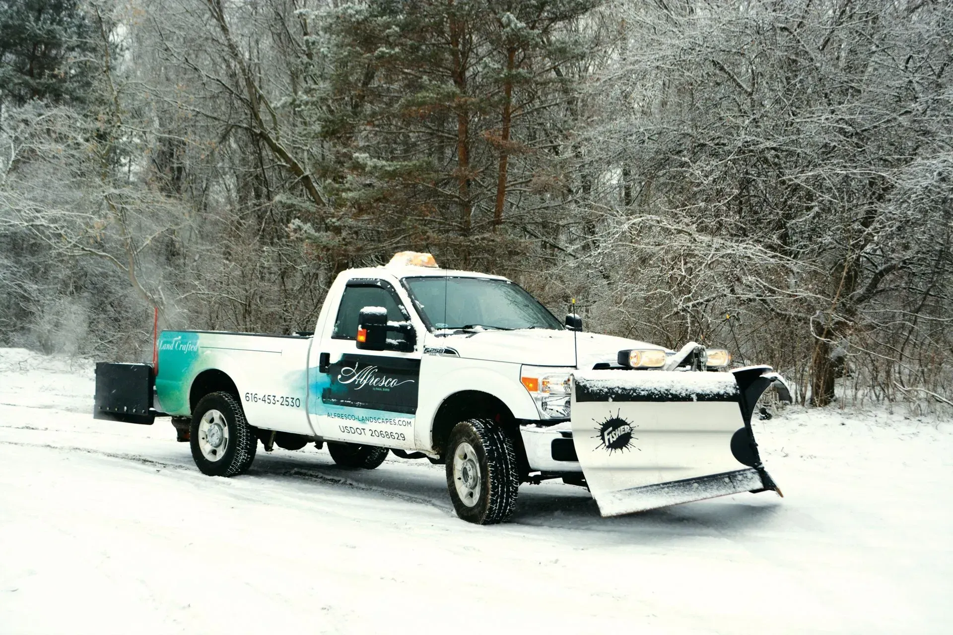Snowplow-equipped white pickup truck driving on a snowy road in a winter forest
