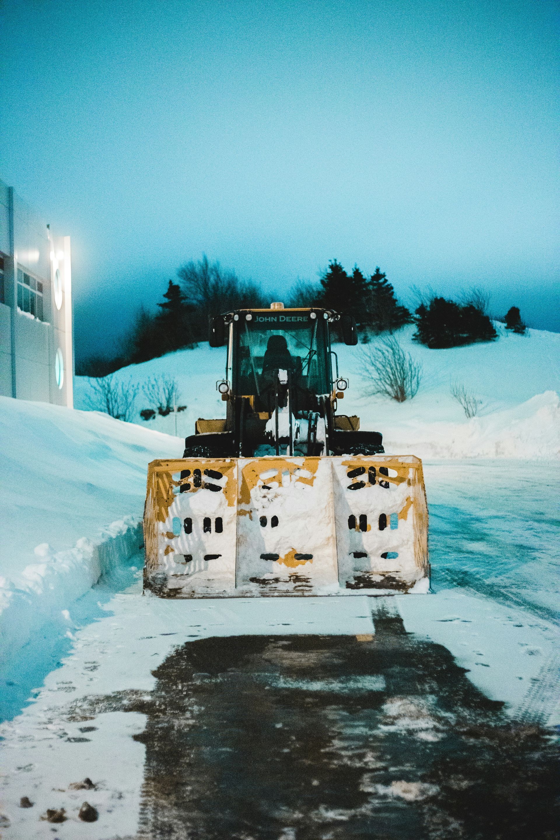 Snowplow clearing a snowy road at dusk, with a yellow plow blade and snowbanks on both sides