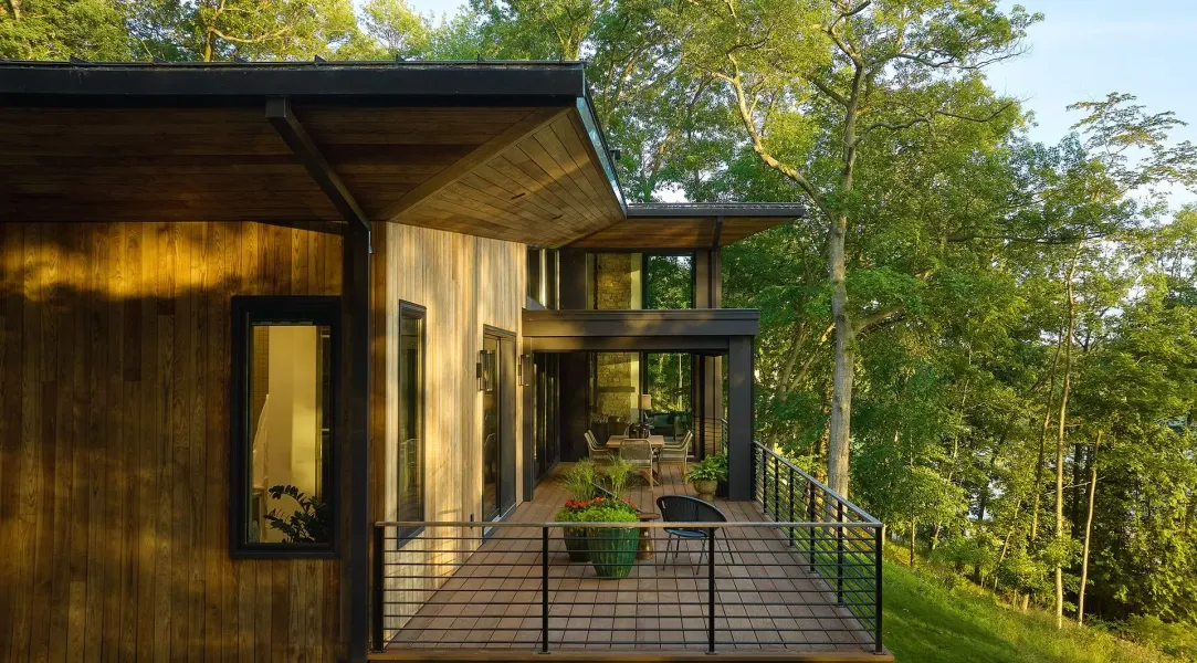 Wooden cabin with a covered deck overlooking a tree-filled landscape.