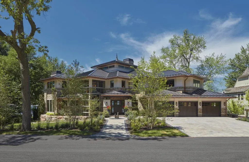 Multi-story luxury home with stone and wood exterior, three-car garage, and blue tile roof, under a blue sky.