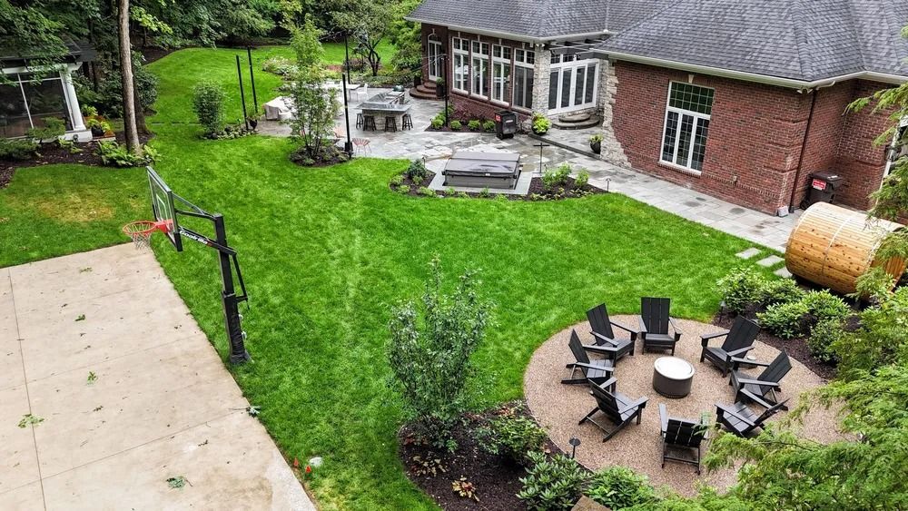Aerial view of backyard with lawn, patio, fire pit, and brick house.