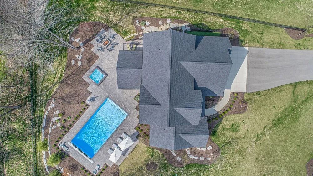 Aerial view of a house with a pool, hot tub, and patio, all surrounded by landscaping.