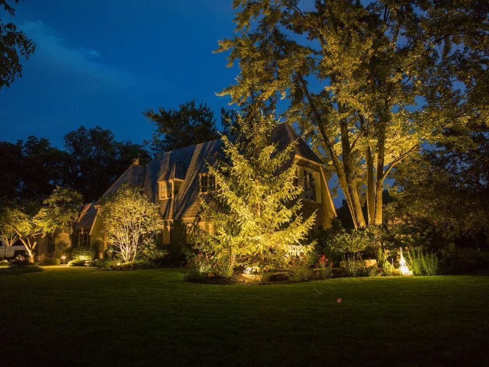 Large house illuminated by outdoor lighting at night.