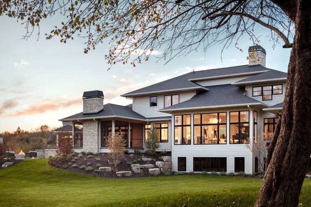 Modern house with large windows, stone accents, and a manicured lawn. Dusk sky with a tree in the foreground.