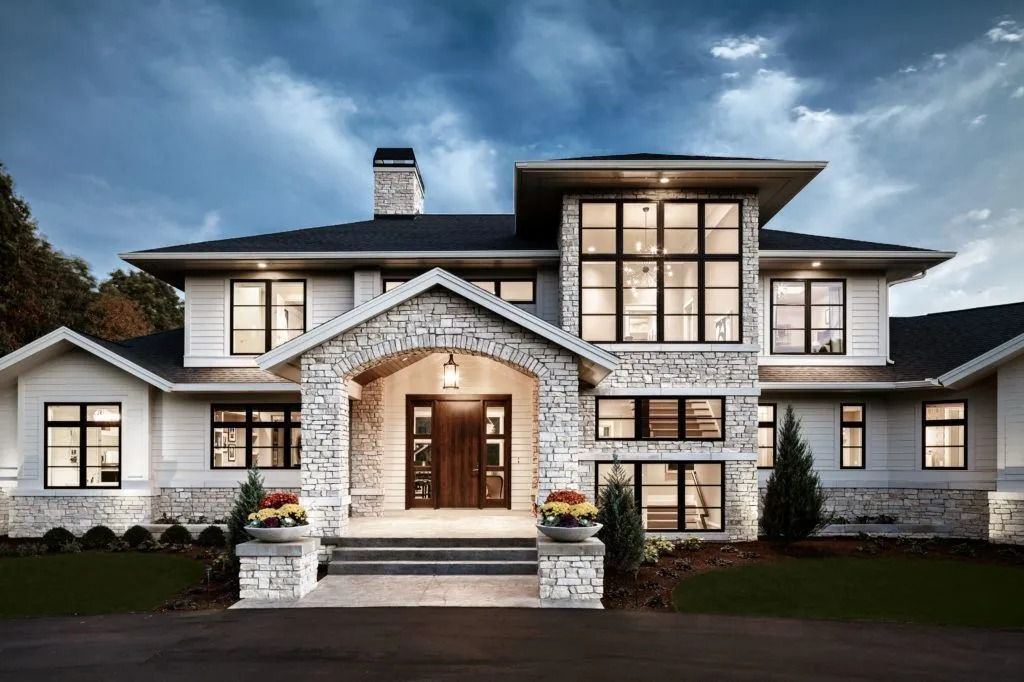 Modern two-story house with stone and white siding, large windows, and an arched entrance under a cloudy sky.