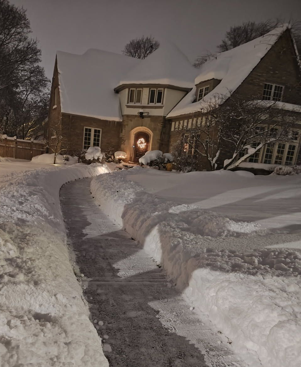 Snow-covered house and walkway at dusk, with a warmly lit arched entrance.