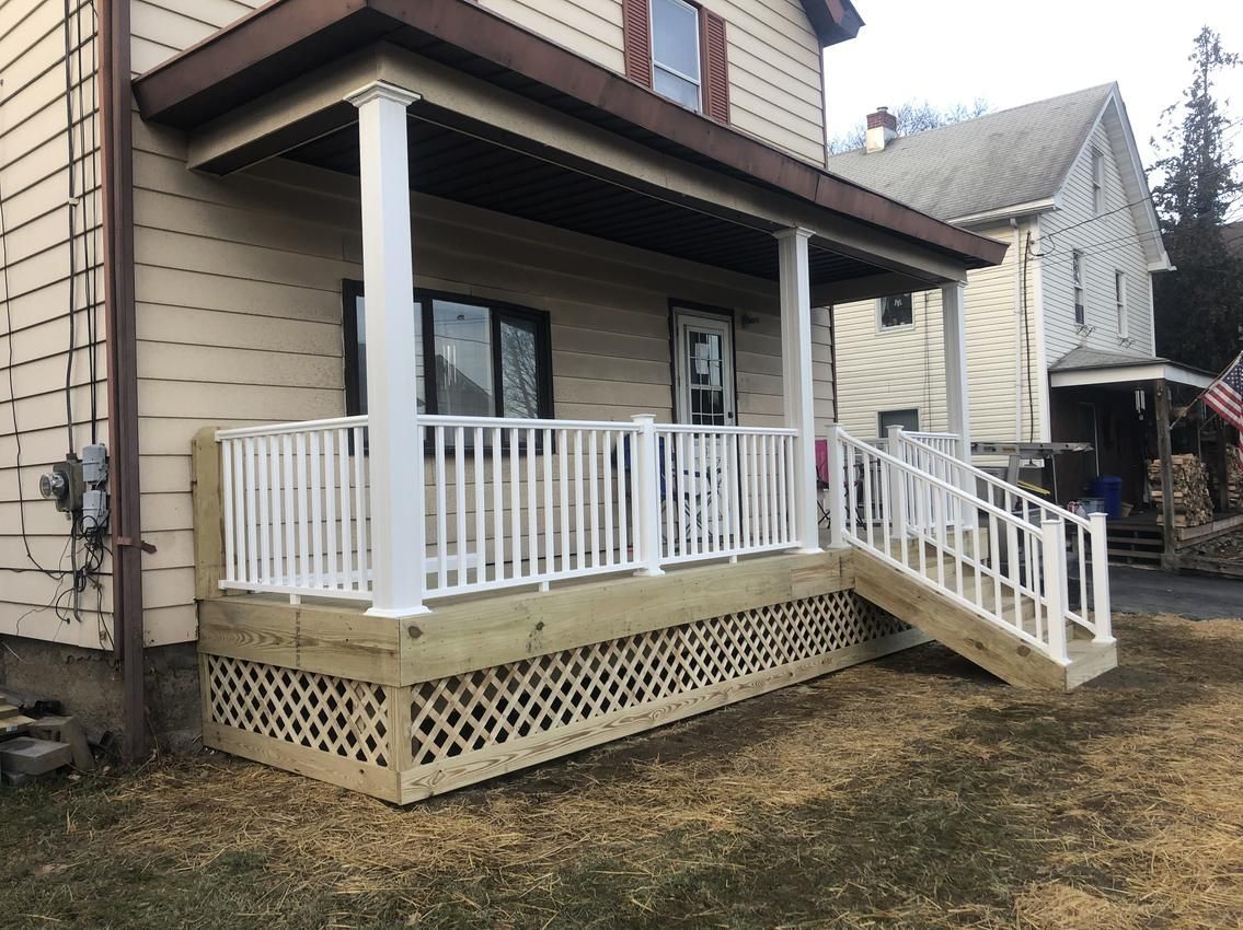 Beige house with a wooden porch and white railings; steps lead to the yard.