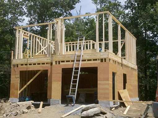 Two-story building under construction with wooden frame, garage doors, ladder.