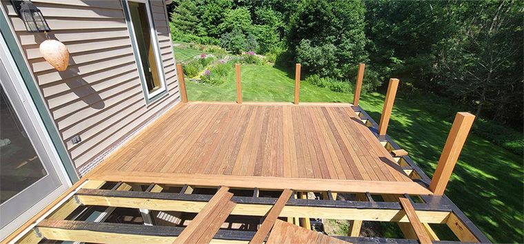 Newly constructed wooden deck with a house in the background and a lush green landscape.