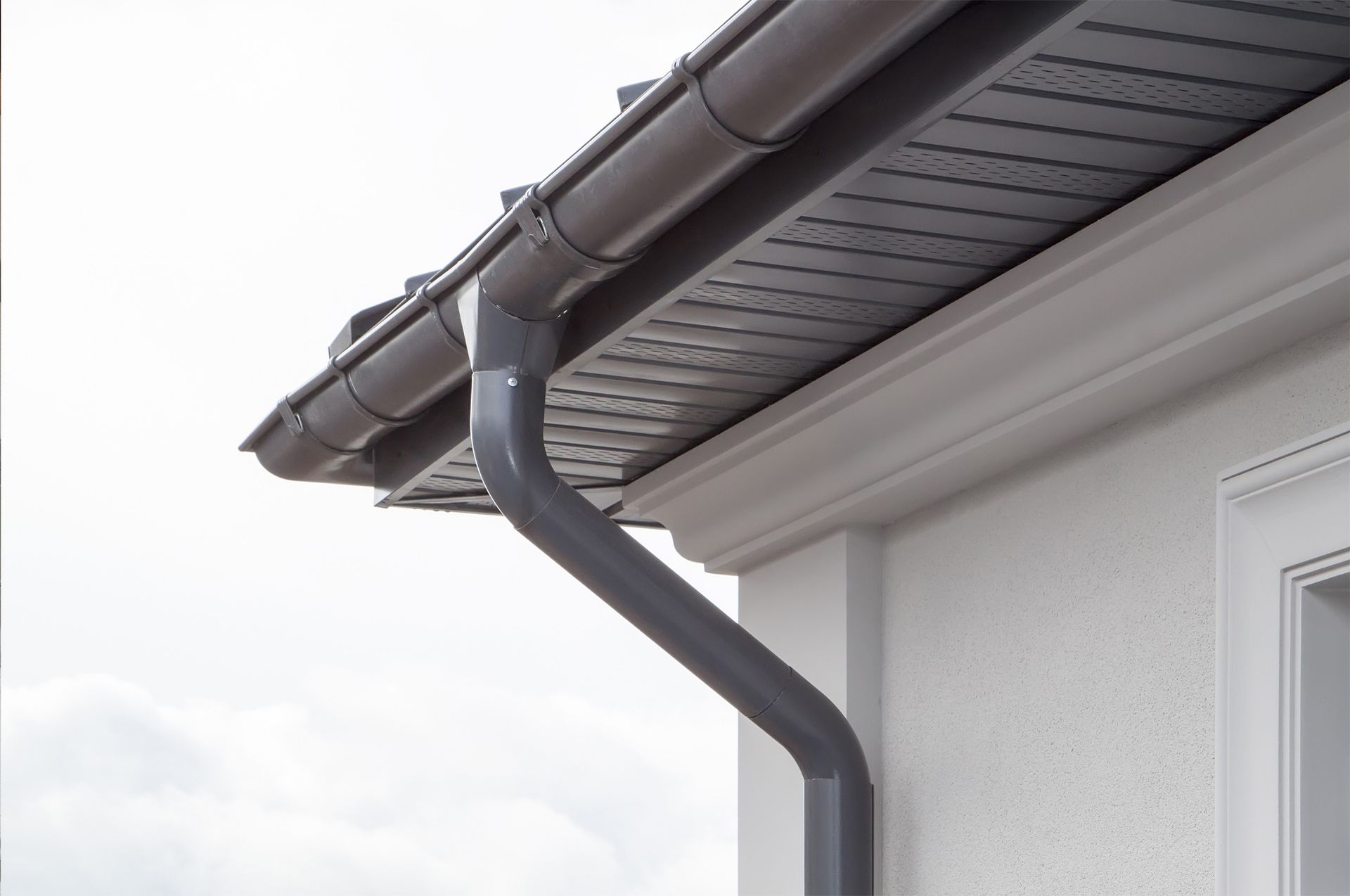Gray gutter system on a white house, against a cloudy sky.