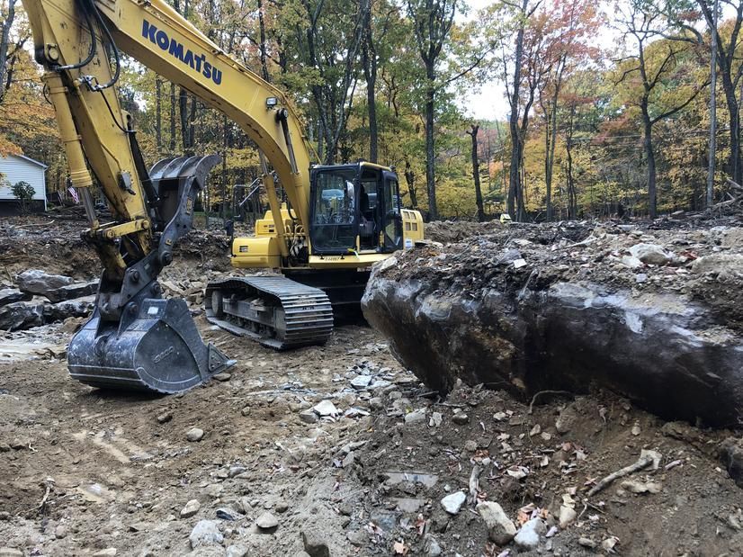 Yellow Komatsu excavator digging earth in a clearing, trees in the background.