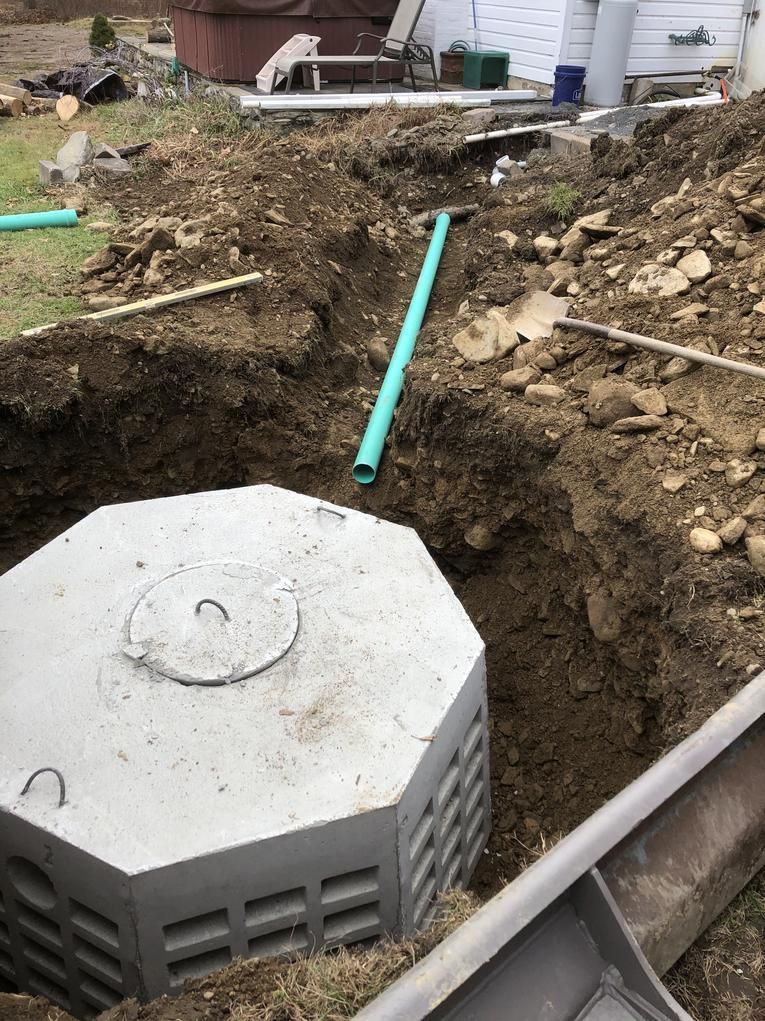 Octagonal concrete structure in a dirt trench, with a green pipe visible. Outdoor setting.