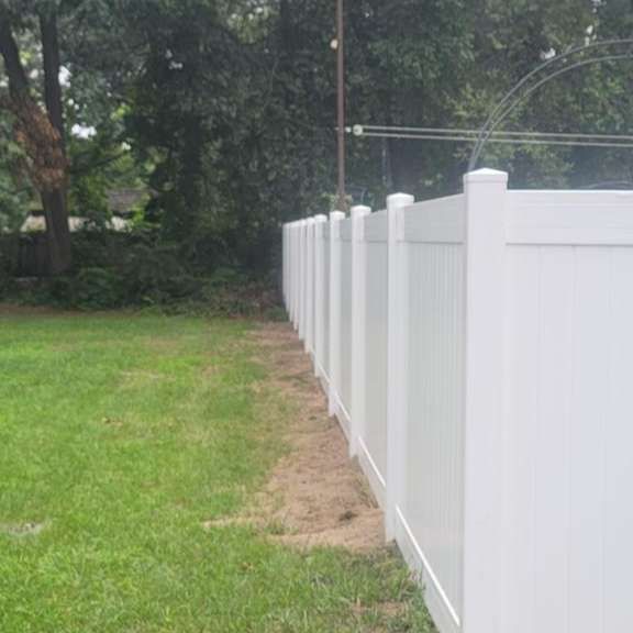 White vinyl fence along grassy yard, with trees in the background.