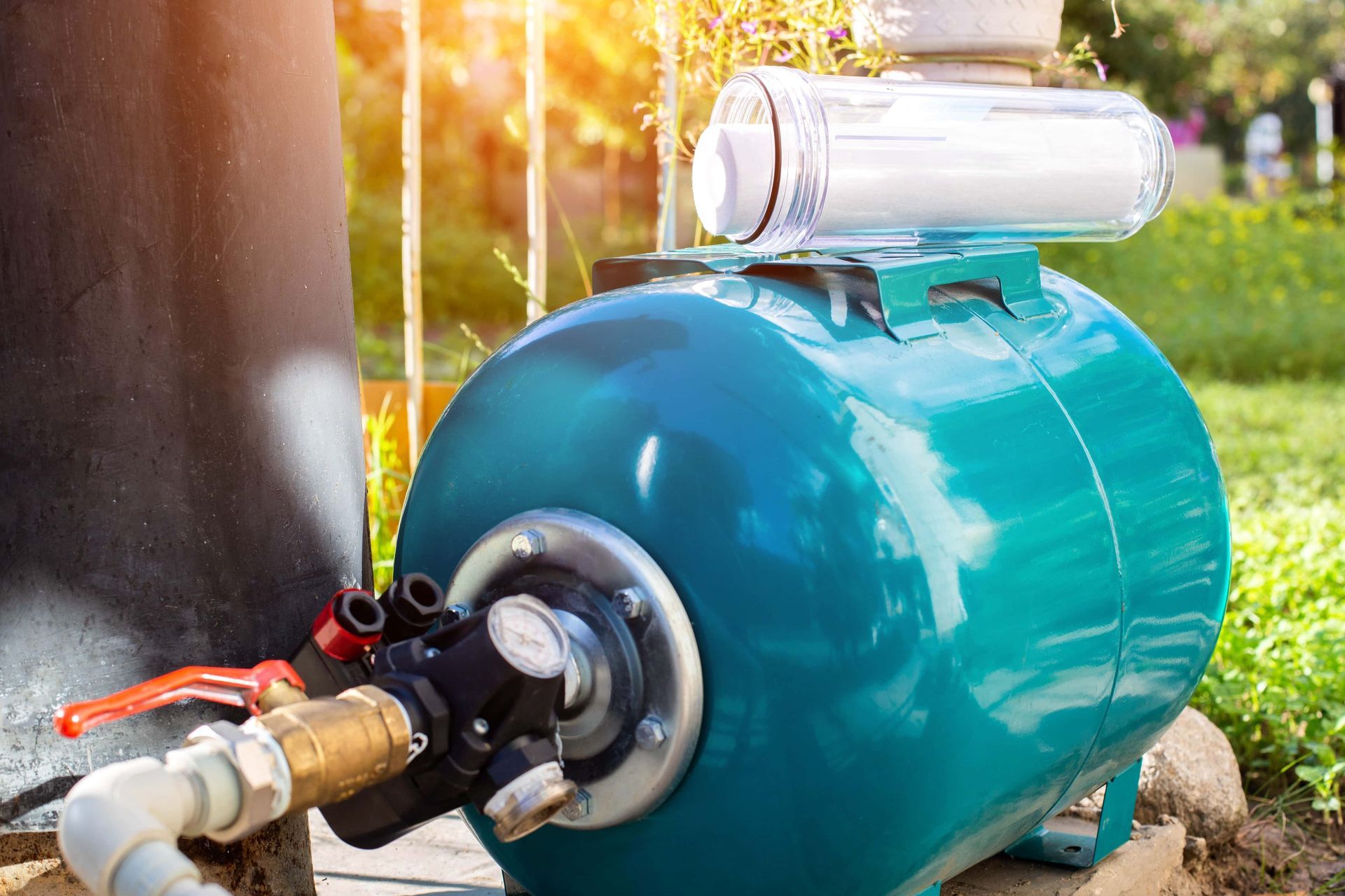 Blue water pressure tank with filter, pipes, and gauge outdoors in sunlight.