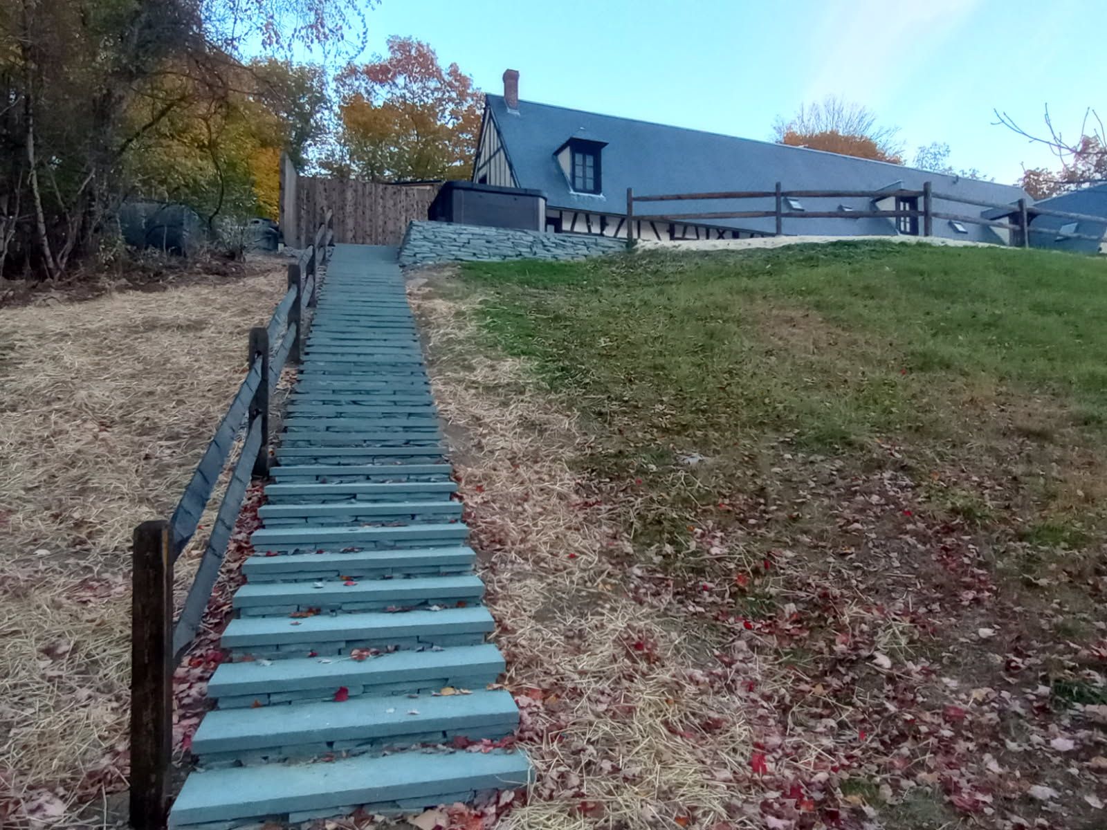 Outdoor staircase leading up a grassy hill to a house. Wooden fence lines both sides of the stairs.