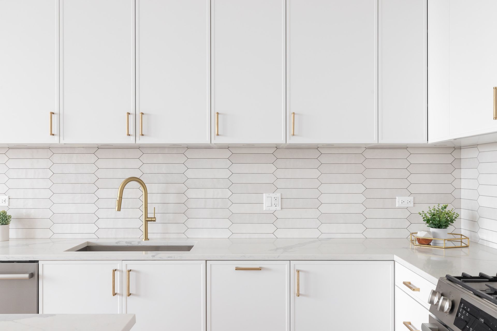 White kitchen with gold fixtures, backsplash tile, and countertops.