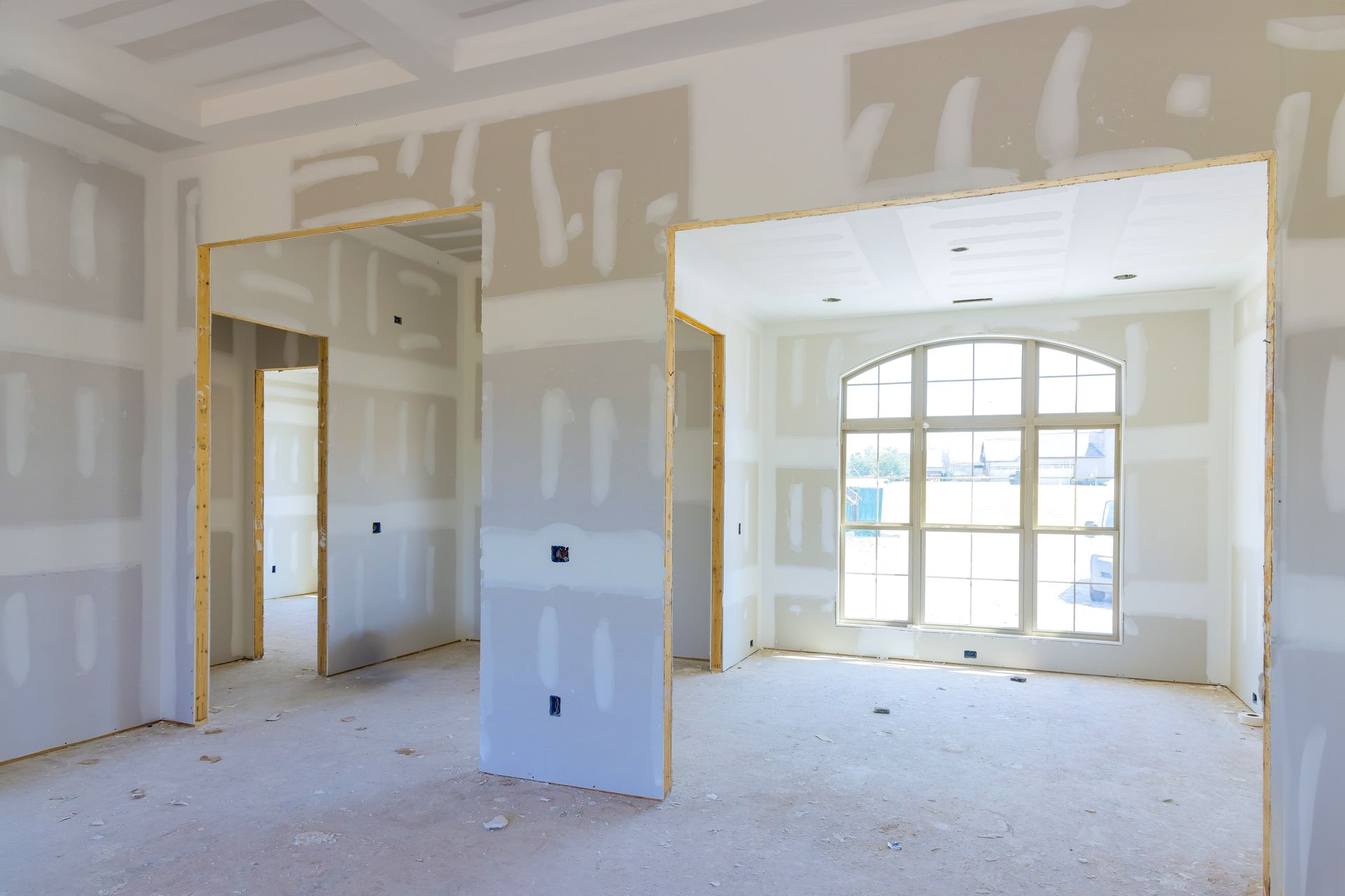 Interior room under construction, with drywall installed, doorway openings, and a large arched window.