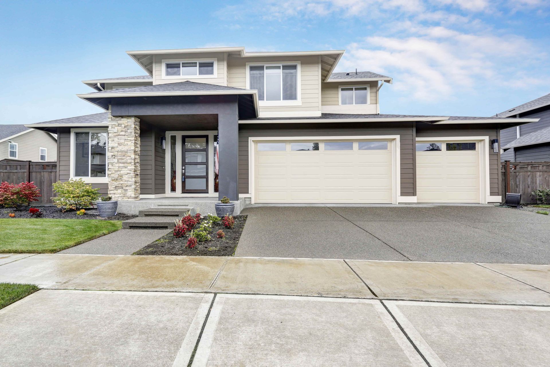 Modern two-story house with tan siding, brown trim, beige garage doors, concrete driveway, and blue sky.
