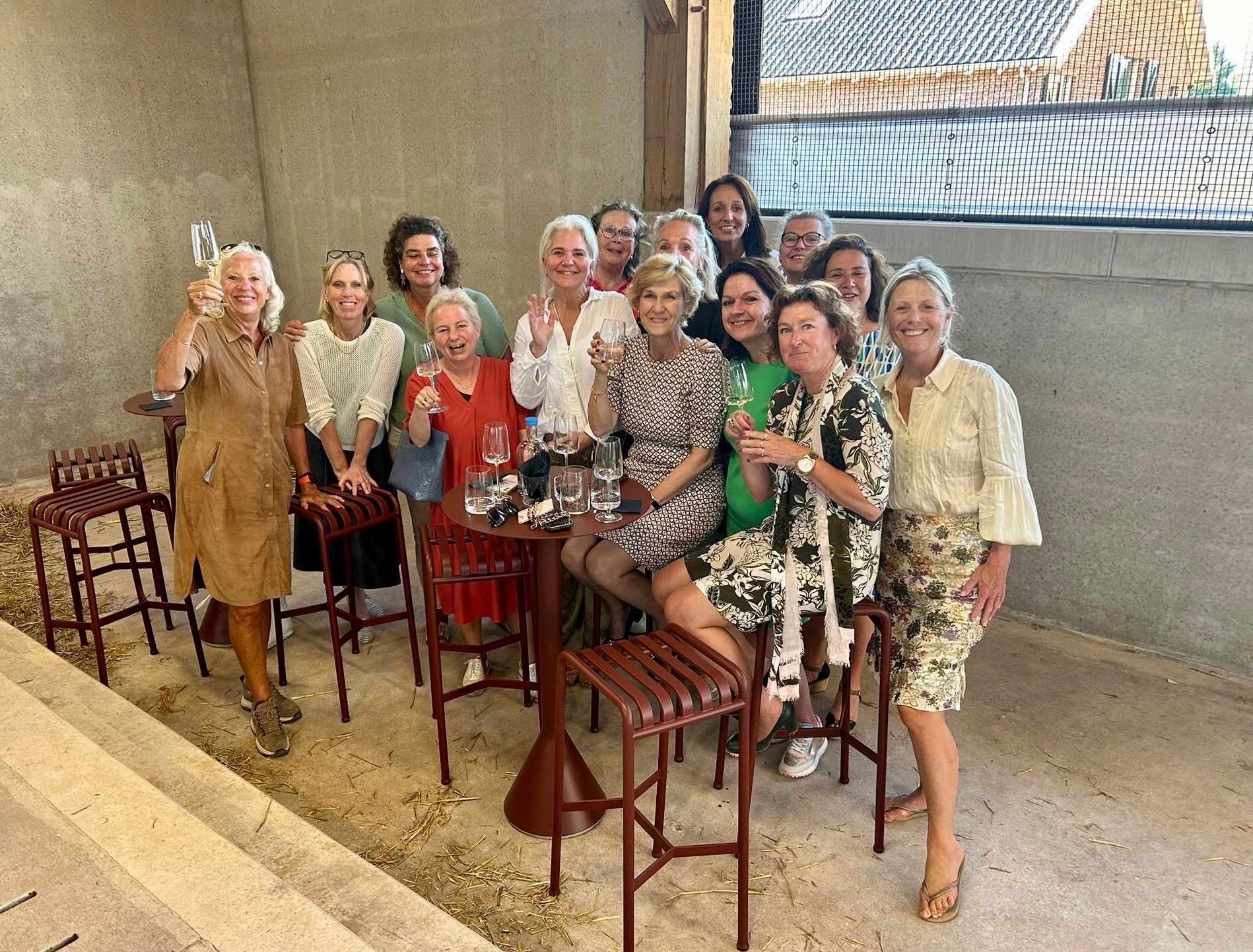 Een groep vrouwen in diverse outfits brengt een champagnetoast uit in een ruimte met stenen muren.