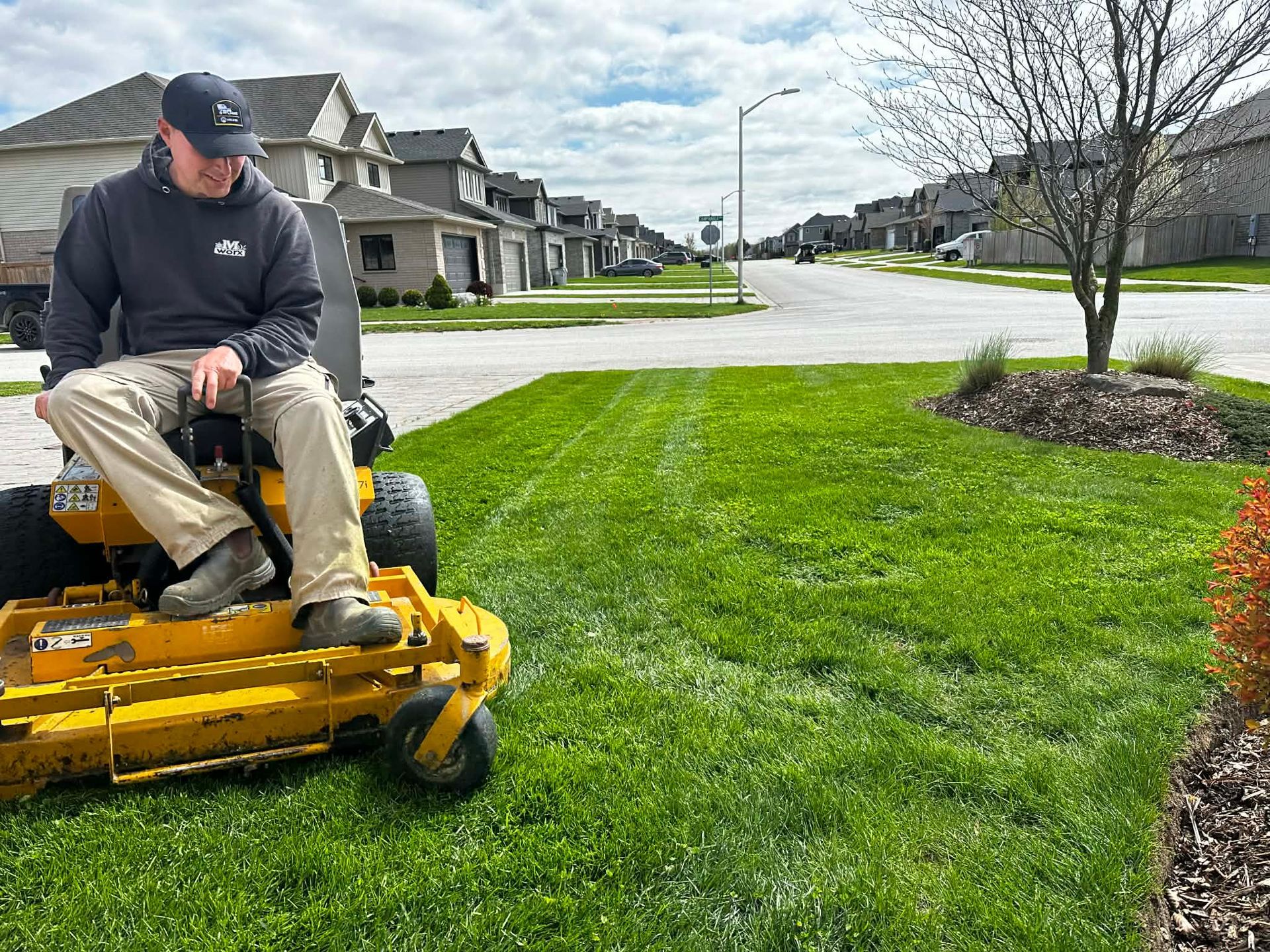 Man mowing a bright green suburban lawn with a yellow riding mower 