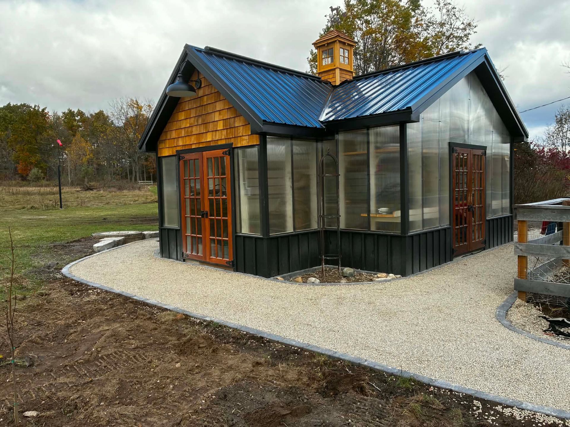 Small modern cabin with blue roof, wood siding, and screened porch on a gravel path outdoors