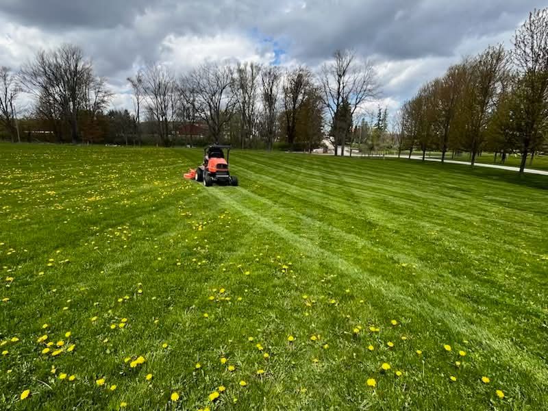 Person mowing a green field under a cloudy sky