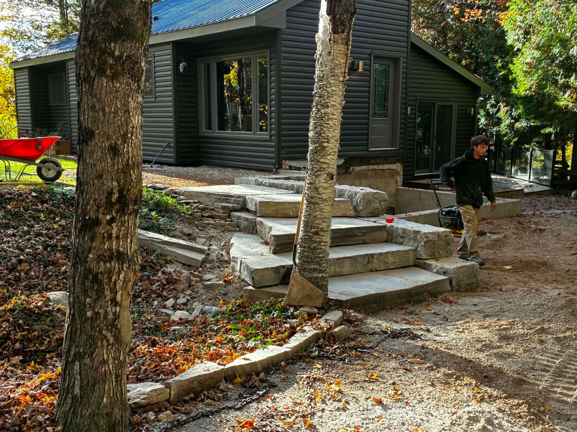 Cabin with stone steps in wooded yard; person walking near the right side.