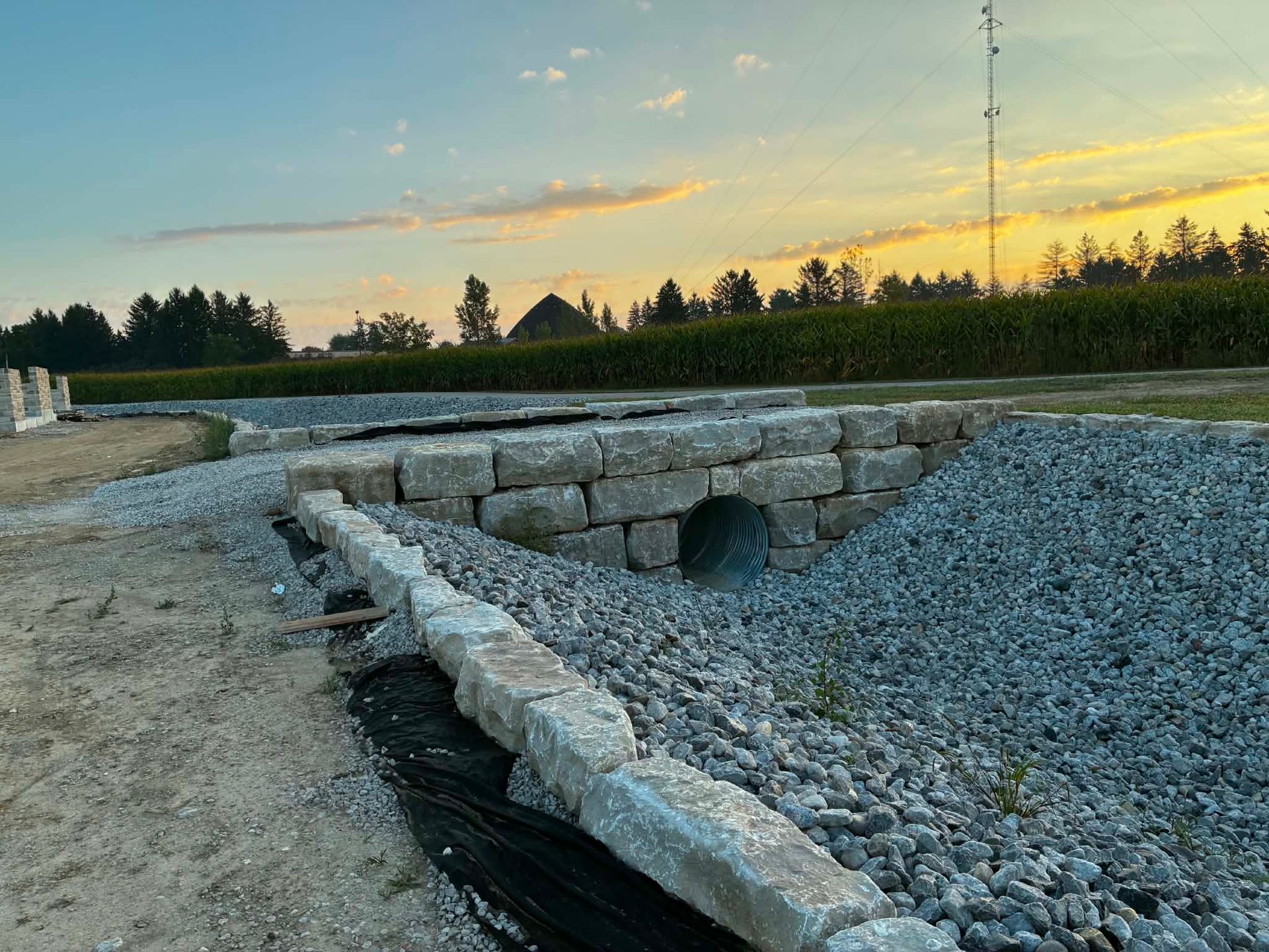 Stone drainage channel under construction beside a gravel road at sunset