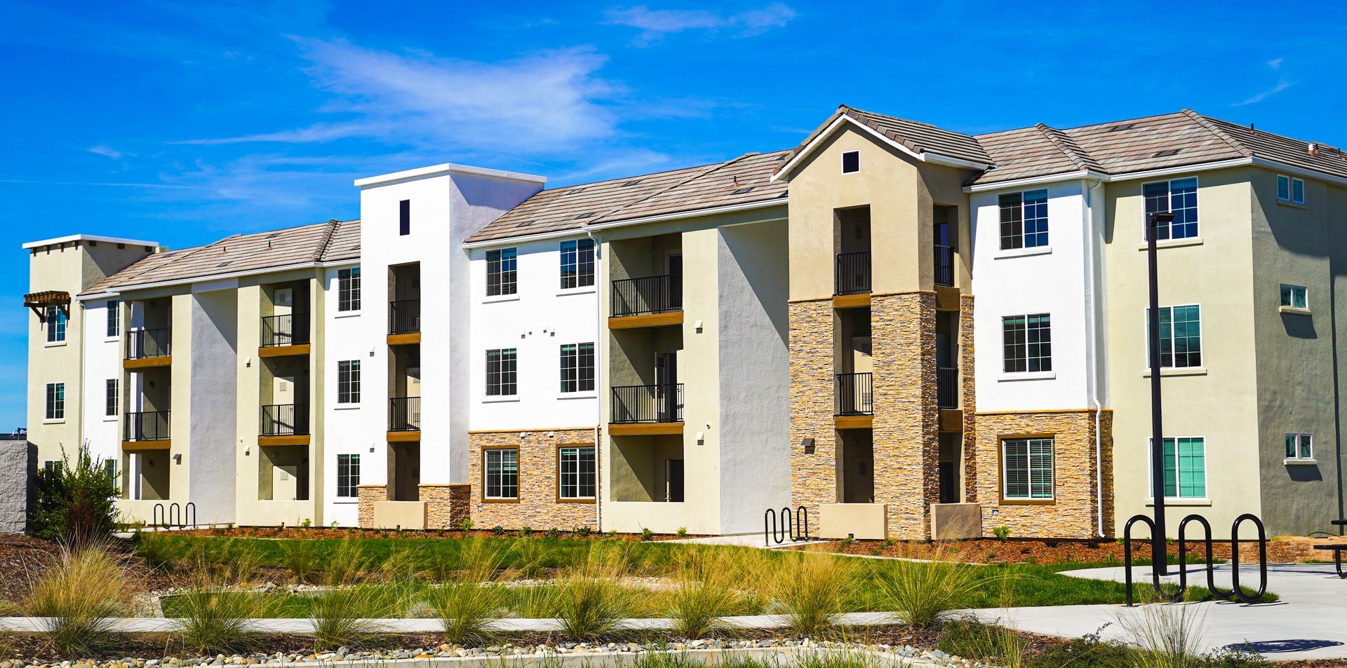 Modern apartment complex with white and beige facades, stone accents, and a blue sky