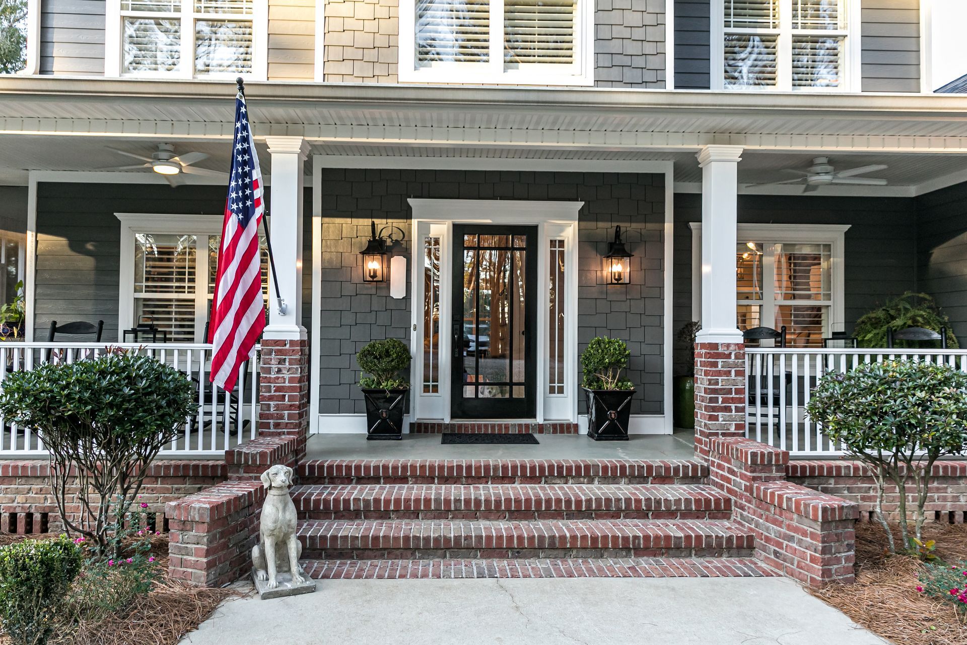 White two-story house with porch and picket fence on a sunny suburban street
