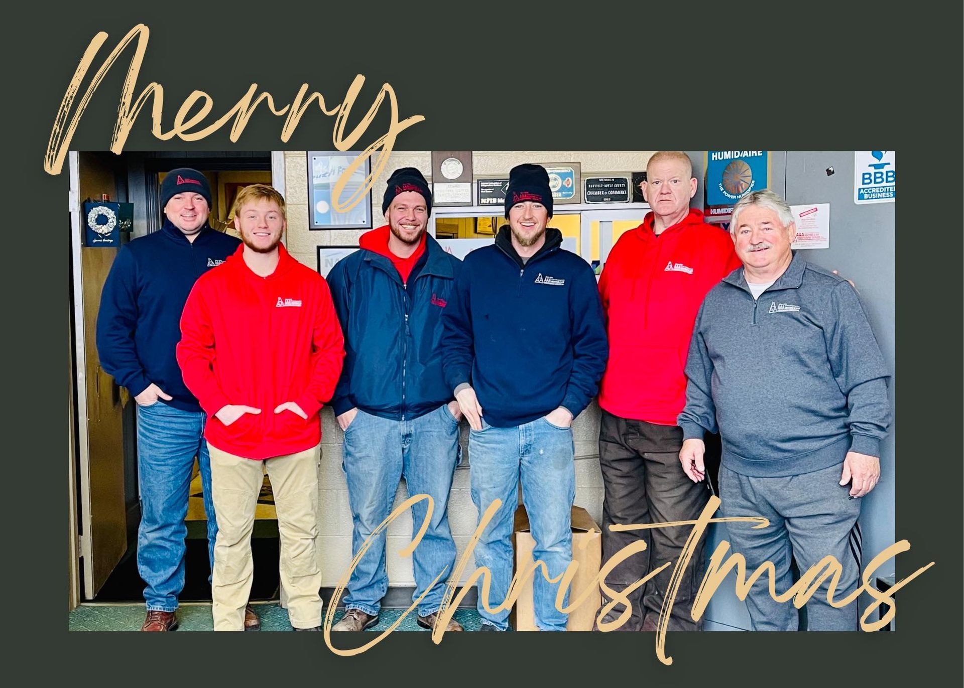 Six people wearing jackets and hats, posing for a Christmas photo. 