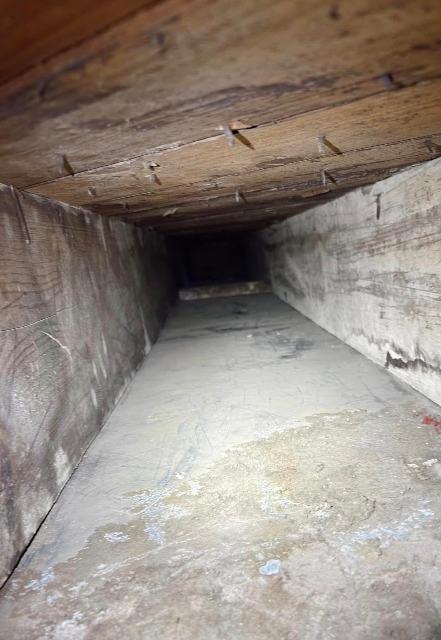 Inside of an air vent, the walls are dusty gray, leading into darkness.