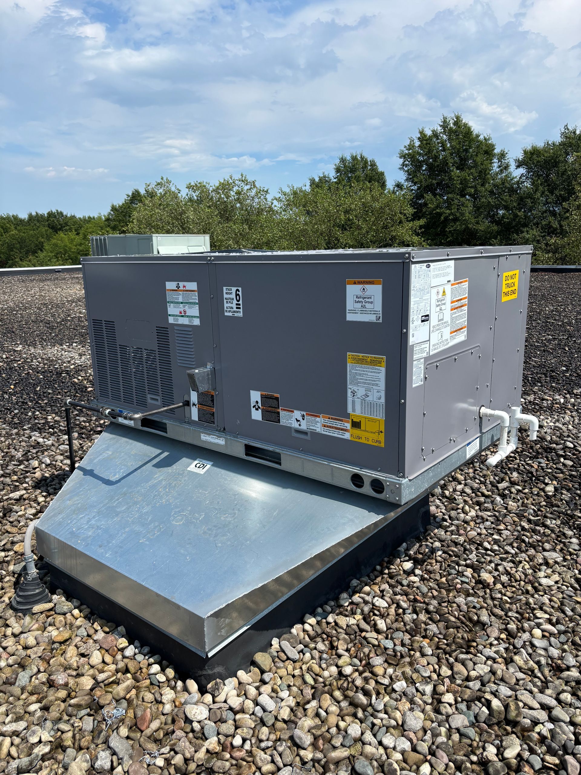 Rooftop HVAC unit on a gravel surface under a partly cloudy sky.