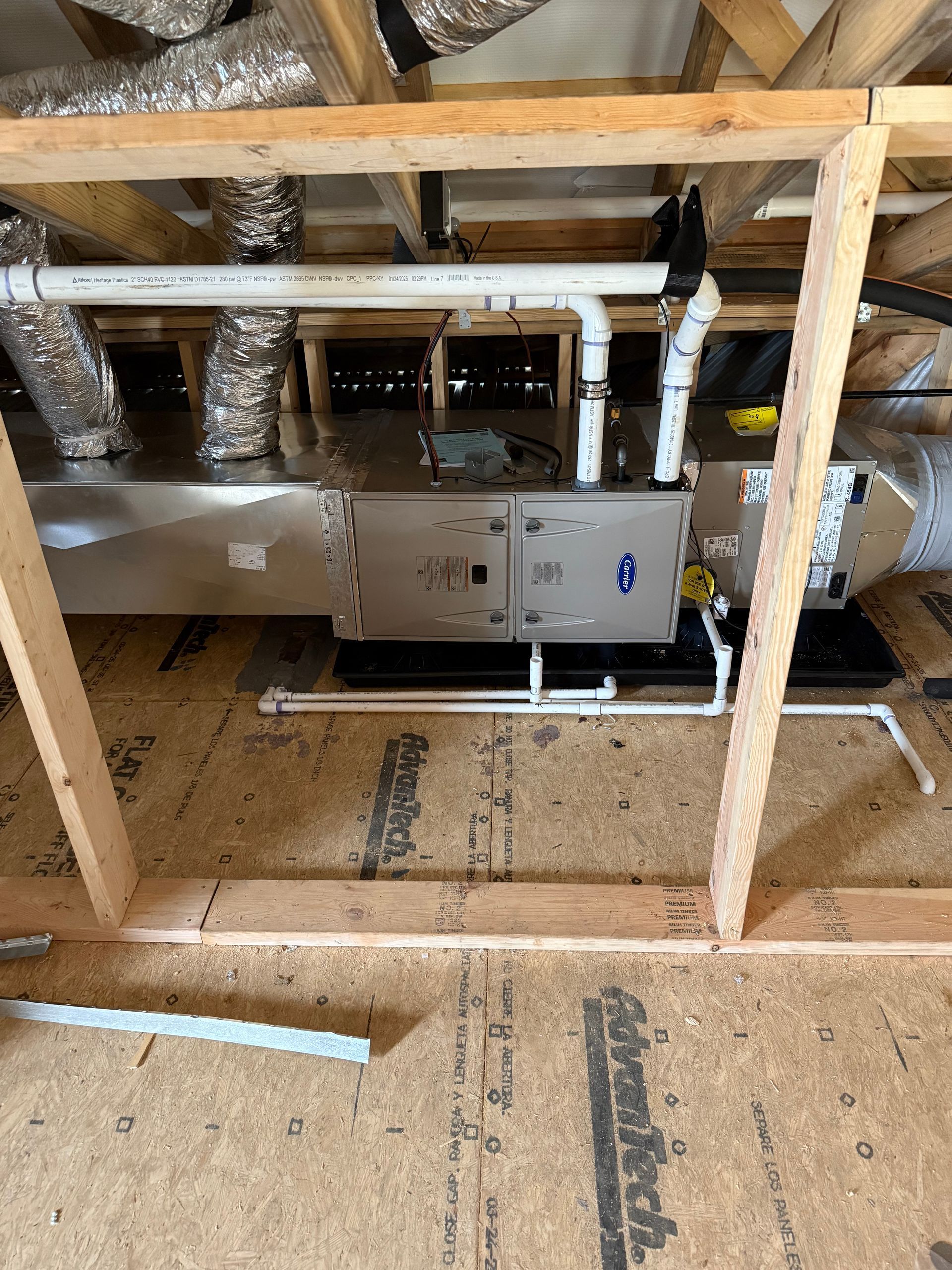 HVAC unit in attic, framed by wood. Ductwork, pipes, and insulation visible.