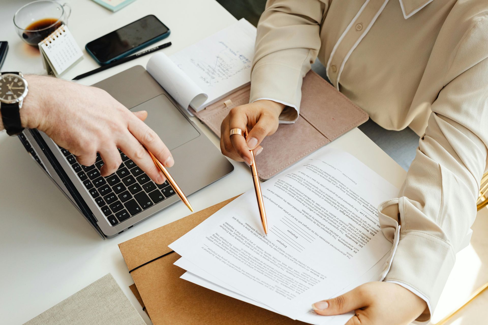 Deux personnes examinent des documents, l'une d'elles utilisant un ordinateur portable et pointant le texte avec des stylos.