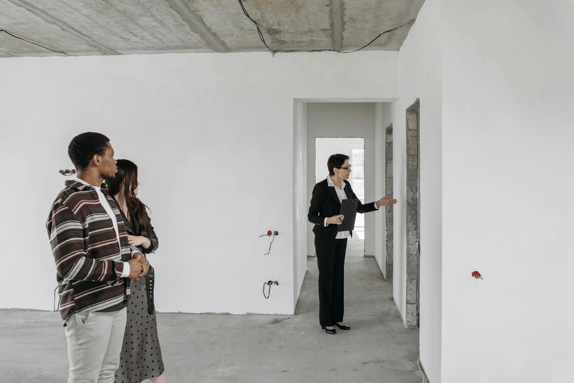 Un couple accompagné d'un agent immobilier visite l'intérieur d'une maison en travaux.