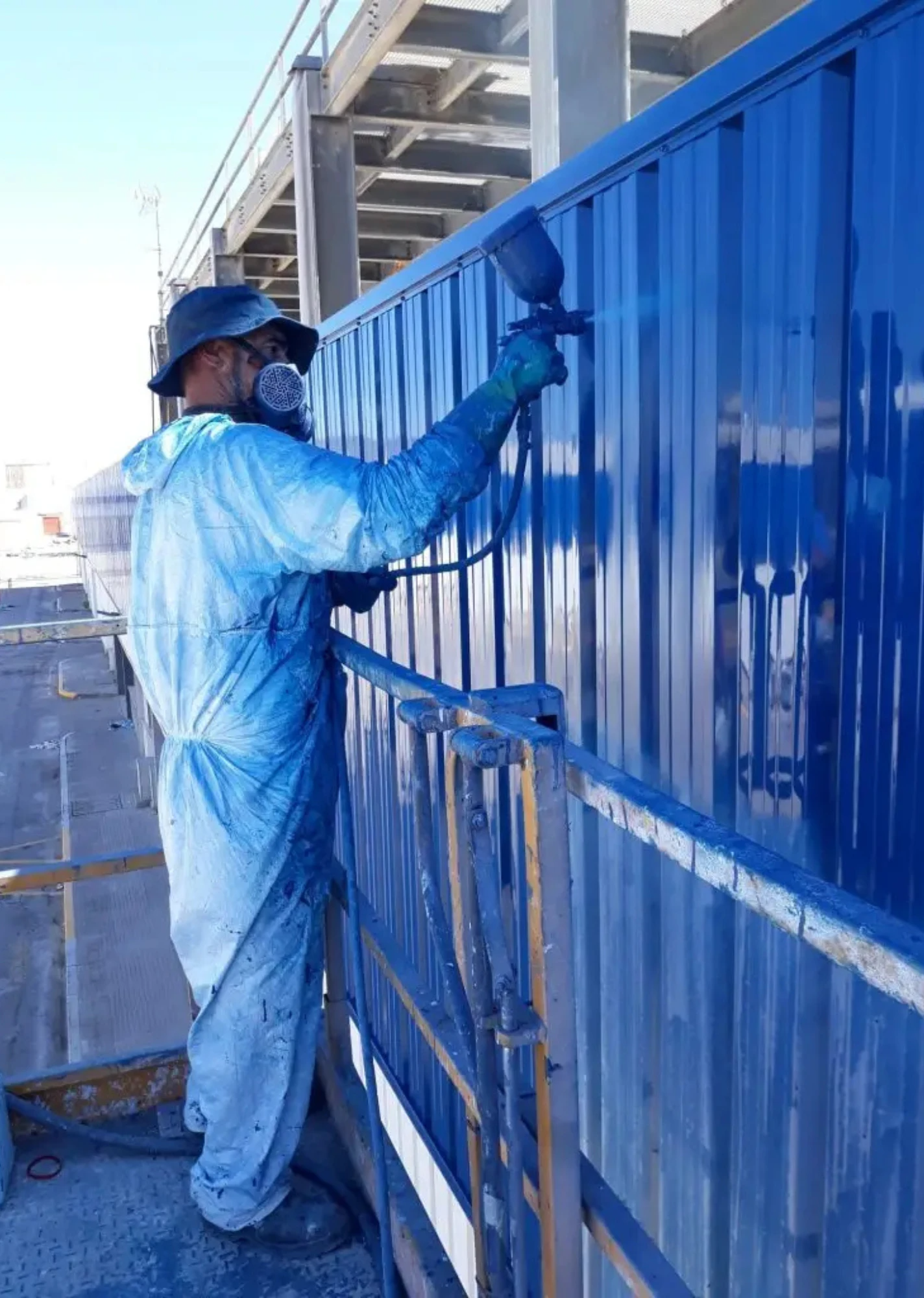 Trabajador con mono azul pintando una pared metálica azul en una obra de construcción