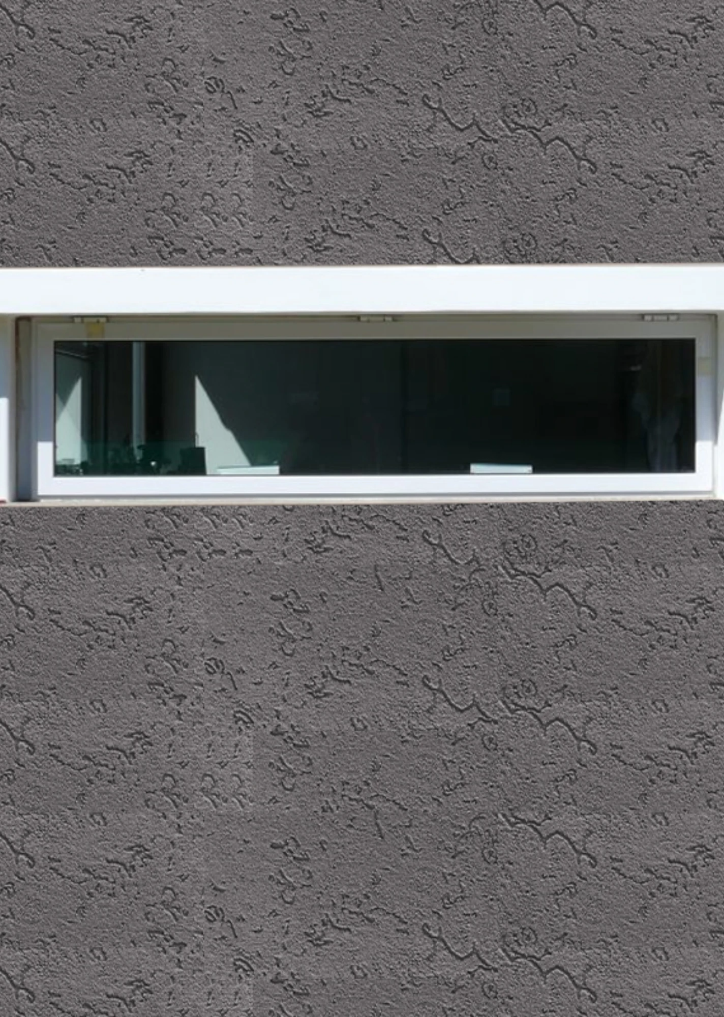 Ventana horizontal estrecha con marco blanco en una pared de estuco gris
