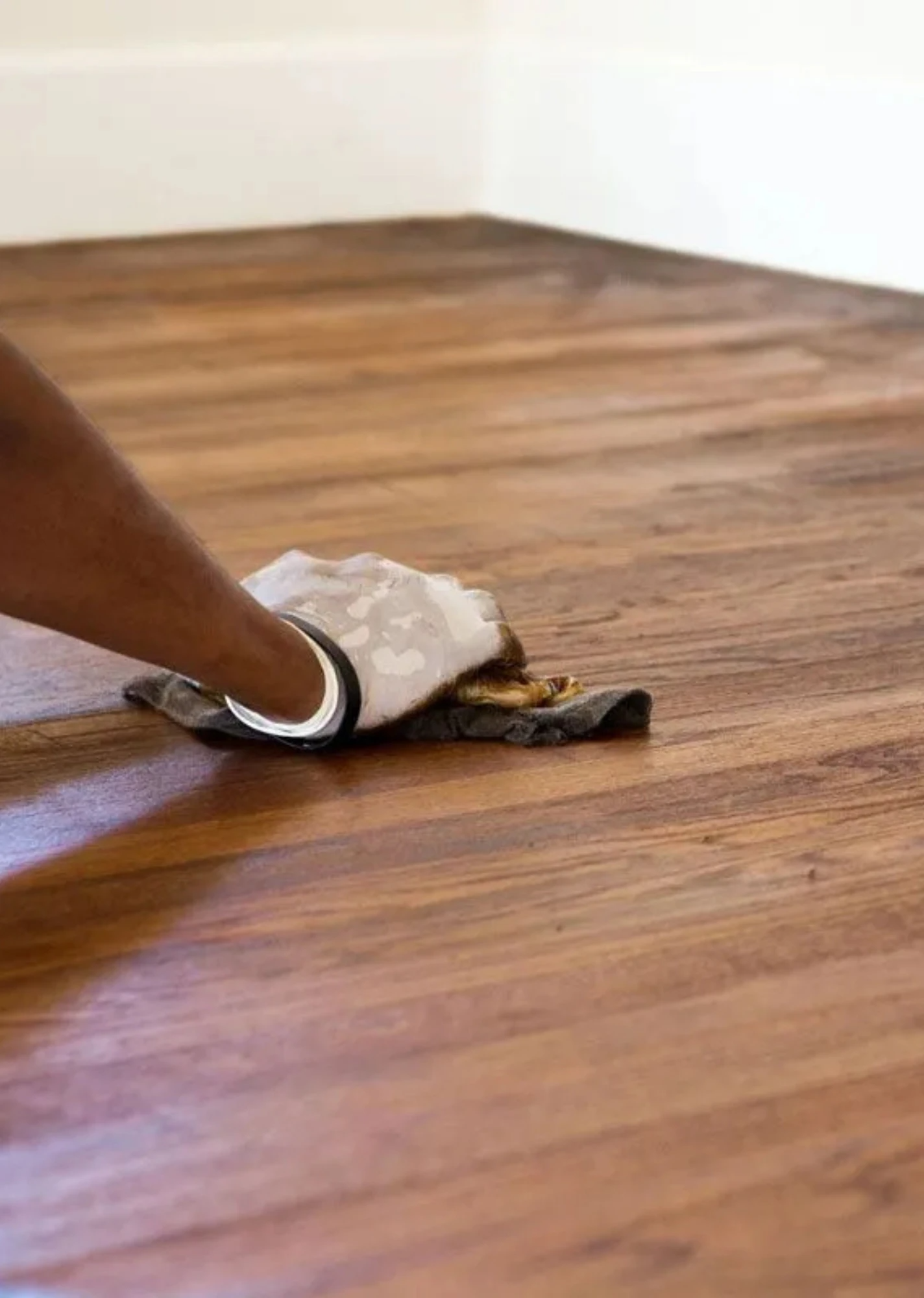 Una mano limpia un suelo de madera marrón con un paño blanco colocado en la mopa
