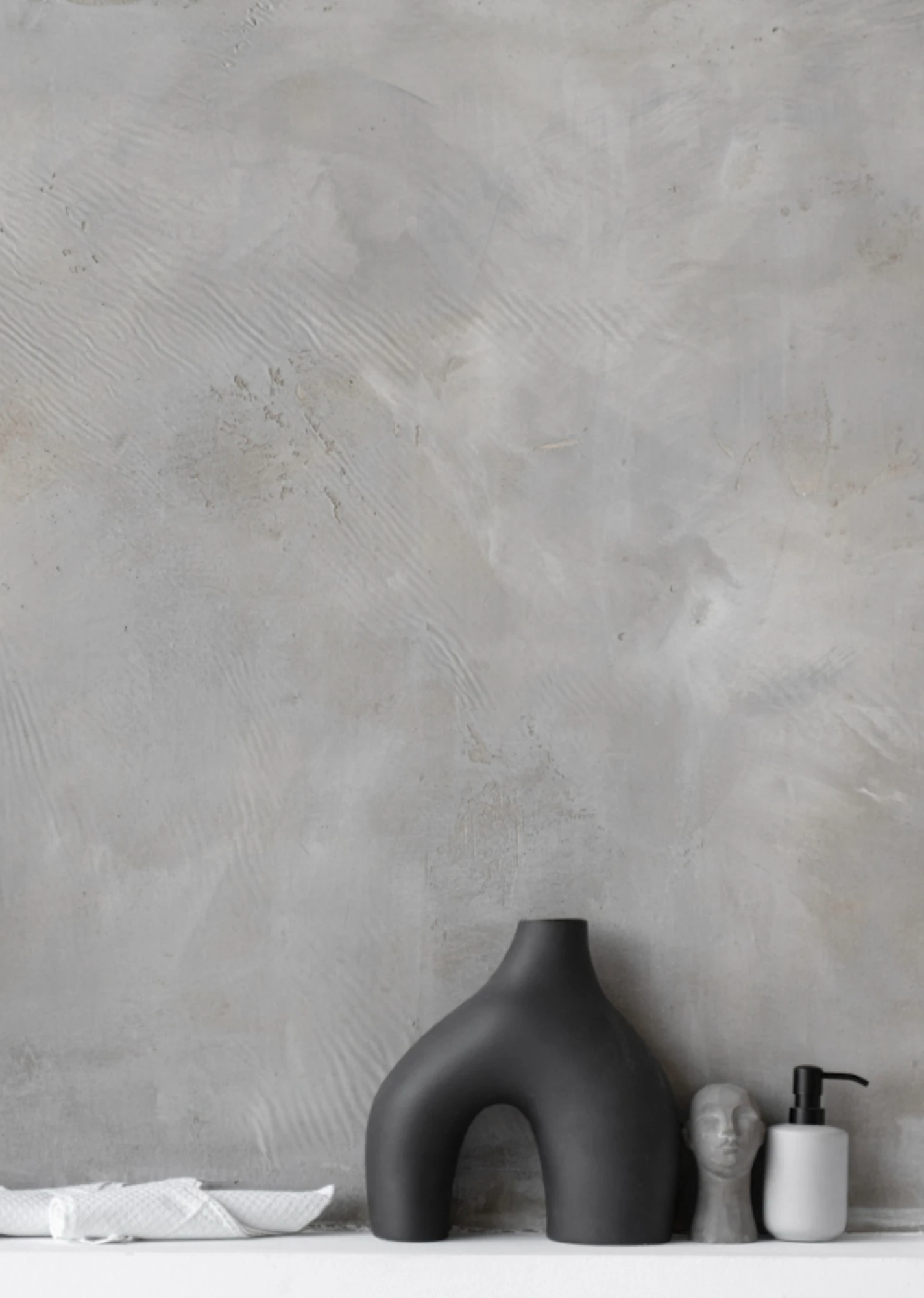 Decoración minimalista para estantería con un jarrón negro arqueado y botellas pequeñas sobre una pared gris texturizada