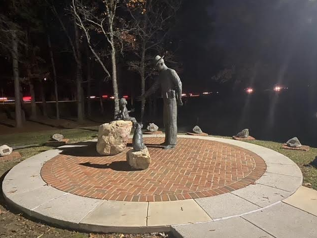Statue of a man with two seals on a circular brick platform, lit at night.