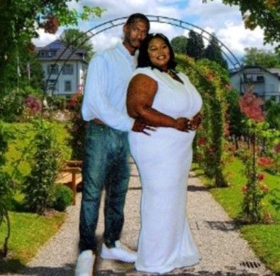 A man and a woman are posing for a picture in a garden . the woman is wearing a white dress.