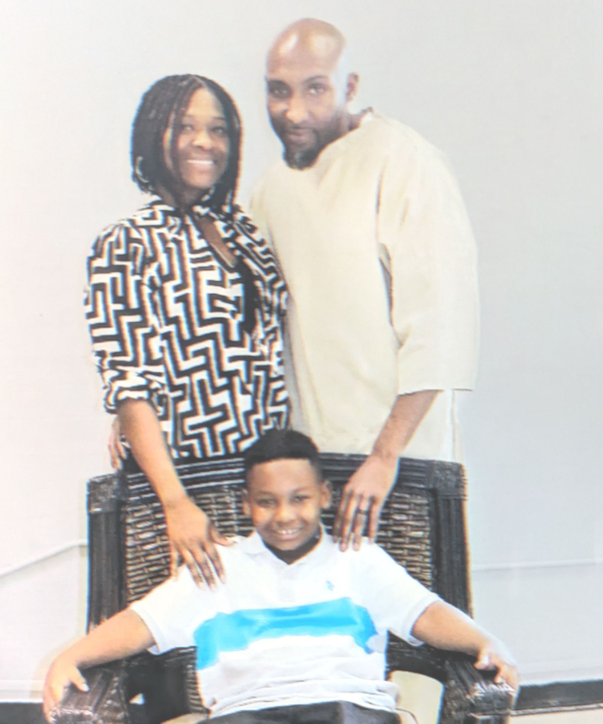 A man and woman are standing next to a boy sitting in a chair.