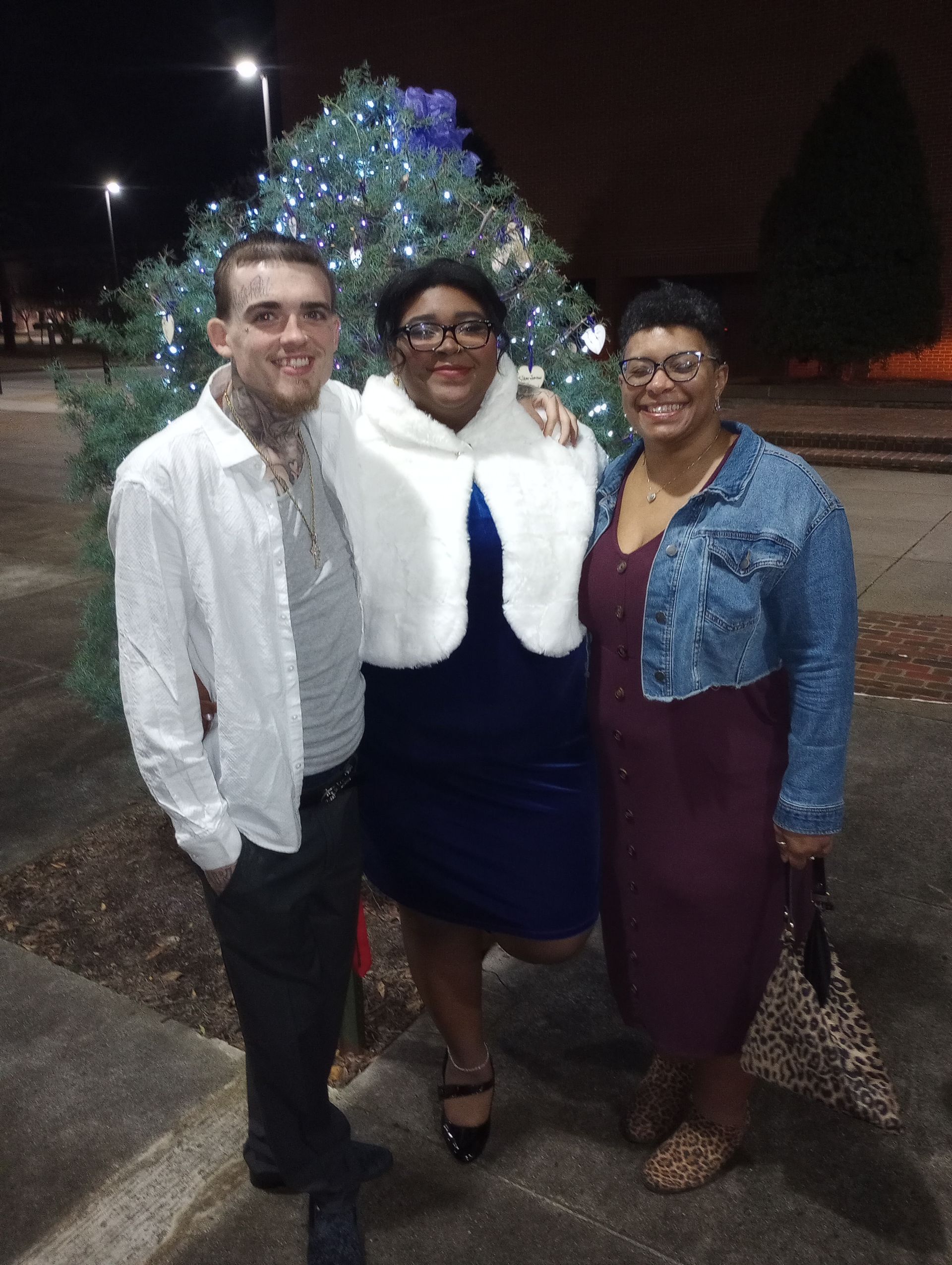 A man and two women are posing for a picture in front of a christmas tree.