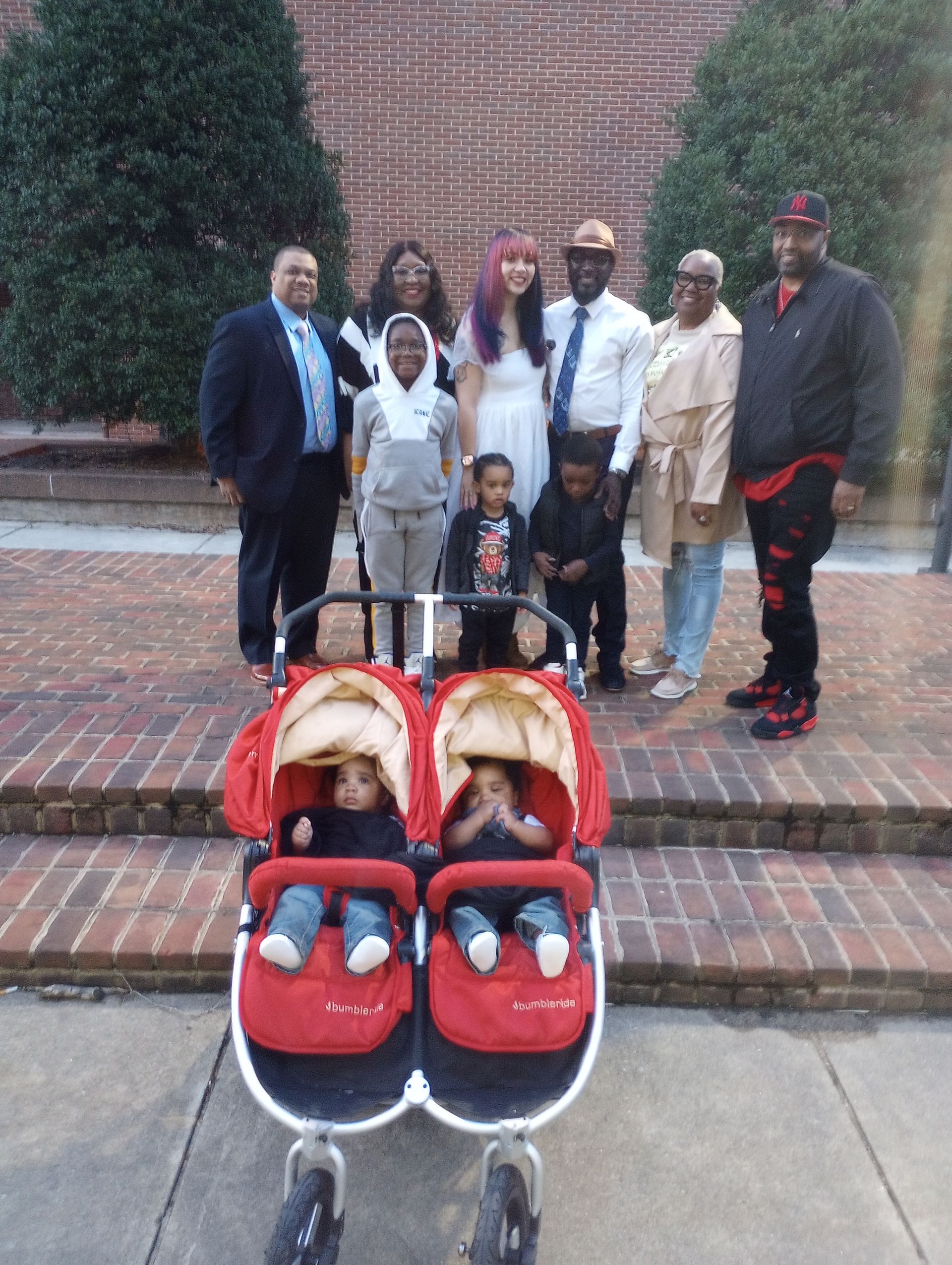 A family posing for a picture with a double stroller