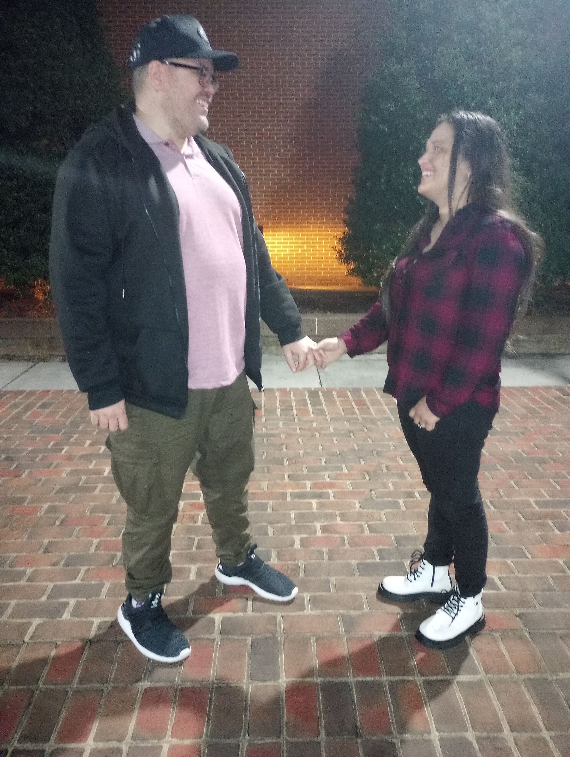 A man and a woman are standing next to each other on a brick sidewalk holding hands.